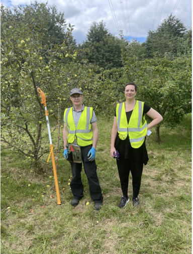 Two individuals in safety vests standing beside a tree with pruning equipment.