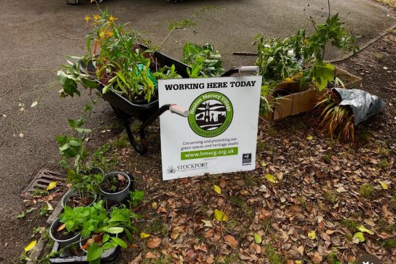 Garden area with potted plants, a wheelbarrow, and a sign promoting a gardening event.